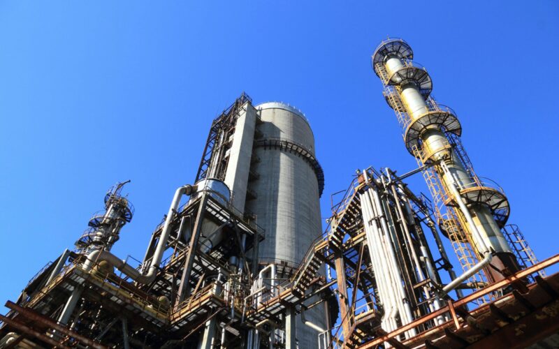 A towering industrial plant under a vivid blue sky, showcasing its intricate architecture and industrial prowess.